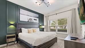 A bedroom with a bed, bedside tables, a desk, a window with blinds, and artwork on the wall.