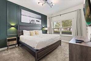 A bedroom with a bed, bedside tables, a desk, a window with blinds, and artwork on the wall.