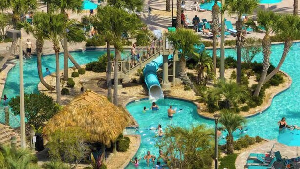 A resort with multiple swimming pools, palm trees, and a water slide.
