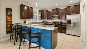 A modern kitchen with dark wood cabinets, a stainless steel refrigerator, and a blue island with bar stools.