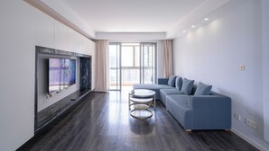 A modern living room with a dark wood floor, a blue sofa, a small round table, and a flat-screen TV mounted on the wall. - Tyms Luxury 3BR 2BA APT Riverside (Shanghai)