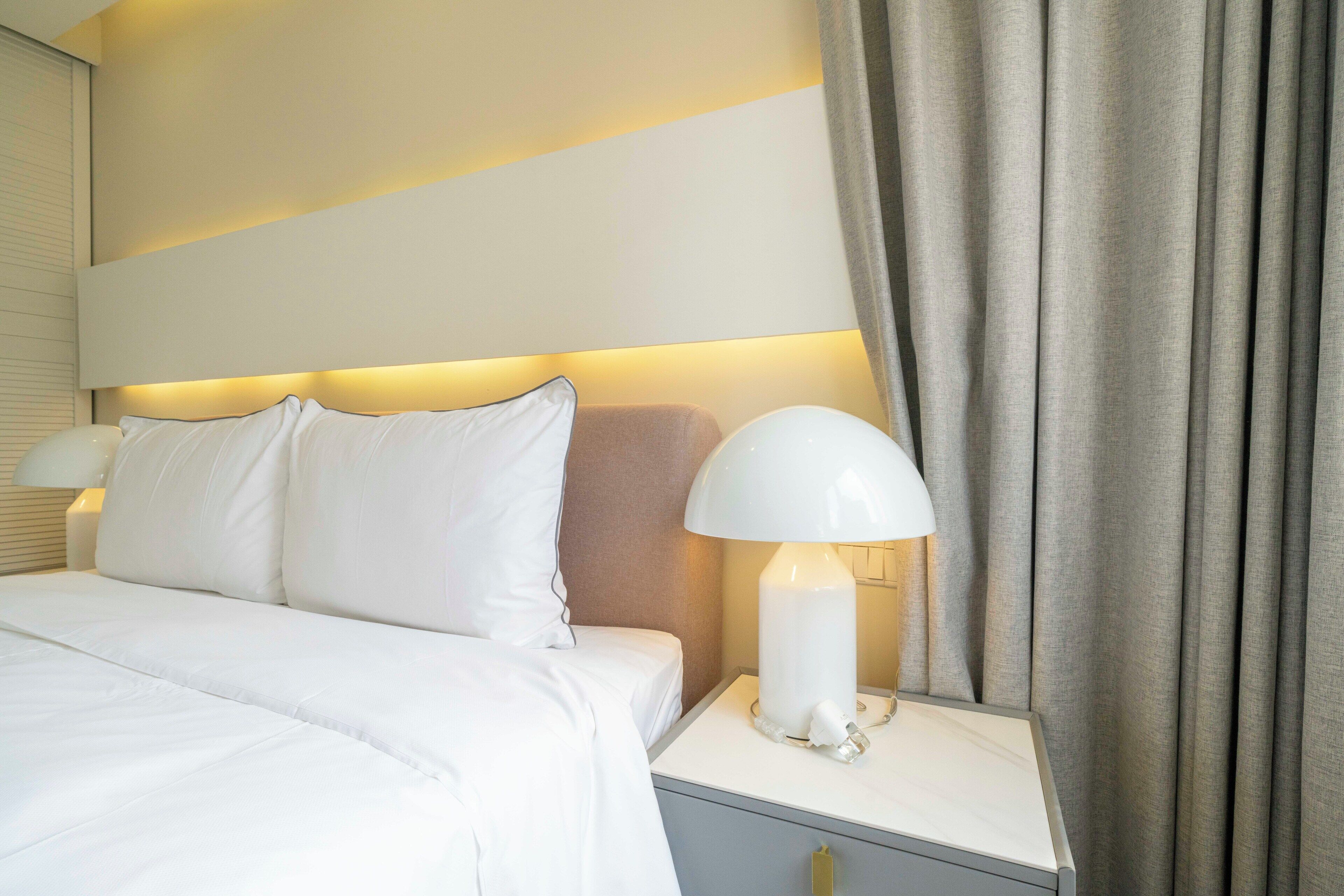 A neatly made bed with white linens, a bedside lamp, and a nightstand with a drawer.