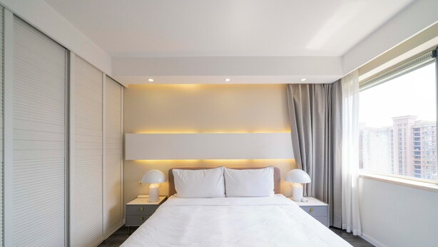 A modern hotel room with a large bed, two bedside tables with lamps, a view of the city through the window, and a sliding door on the left. - Tyms Luxury 3BR 2BA APT Riverside (Shanghai)