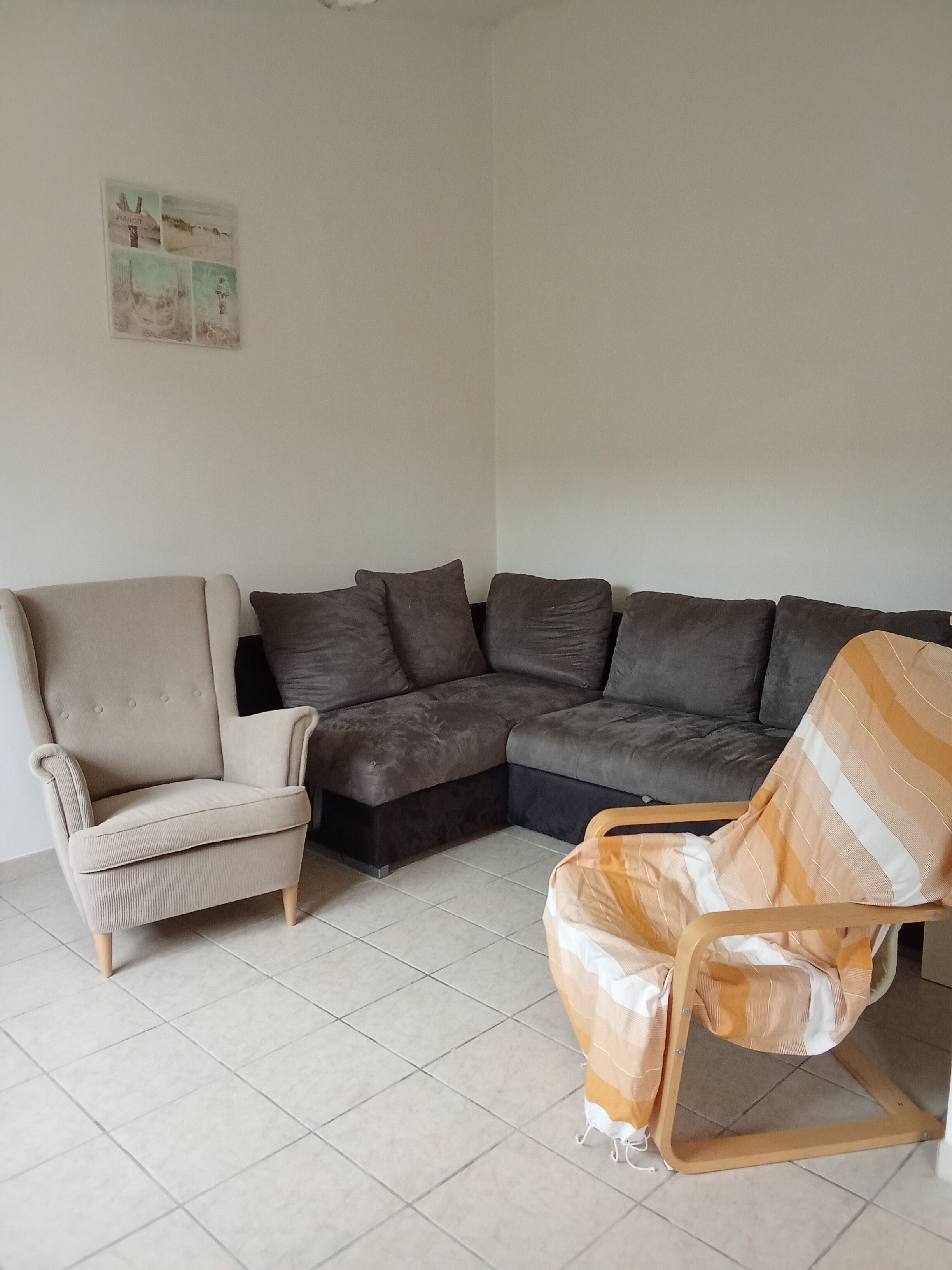 Una sala de estar con un sillón color crema, un sofá seccional marrón oscuro y un sillón a rayas.
