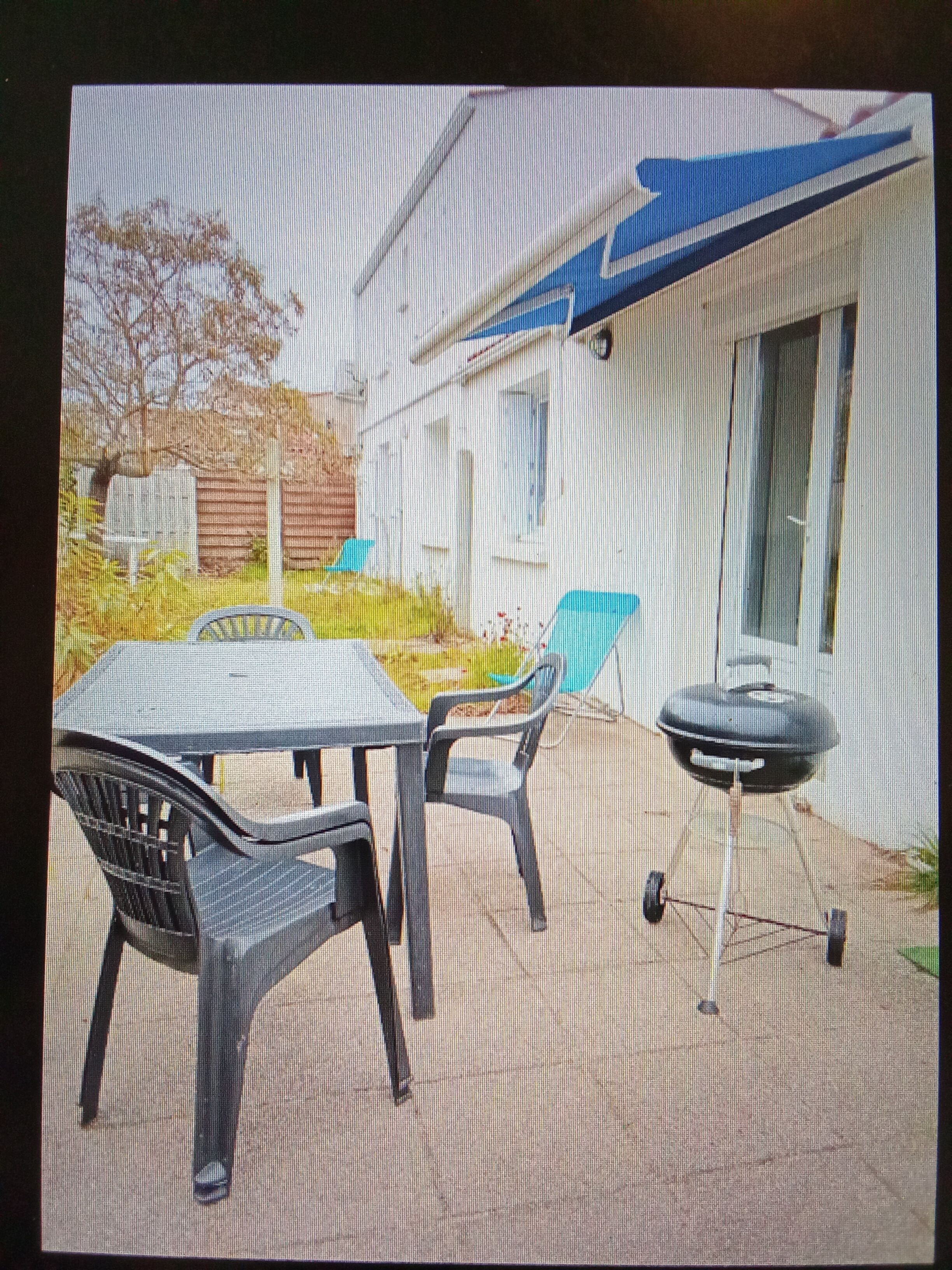 An outdoor patio with a table and chairs, a barbecue grill, and a house in the background.