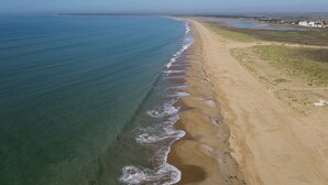 An aerial view of a coastal beach with a clear shoreline, a sandy beach, and a distant view of a town with buildings. - Vendée farmhouse near beach and town center (L'Aiguillon-la-Presqu'île)