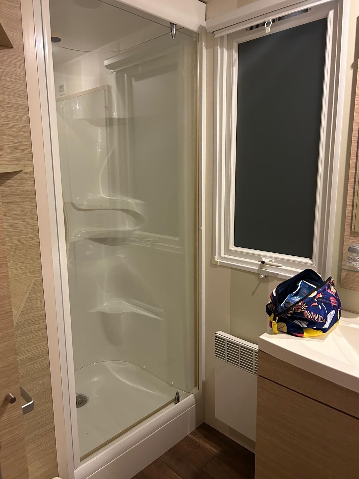 A bathroom with a glass-enclosed shower, a window, and a towel rack.