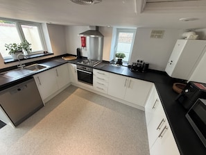A modern kitchen with white cabinets, a stainless steel range hood, and a black countertop.