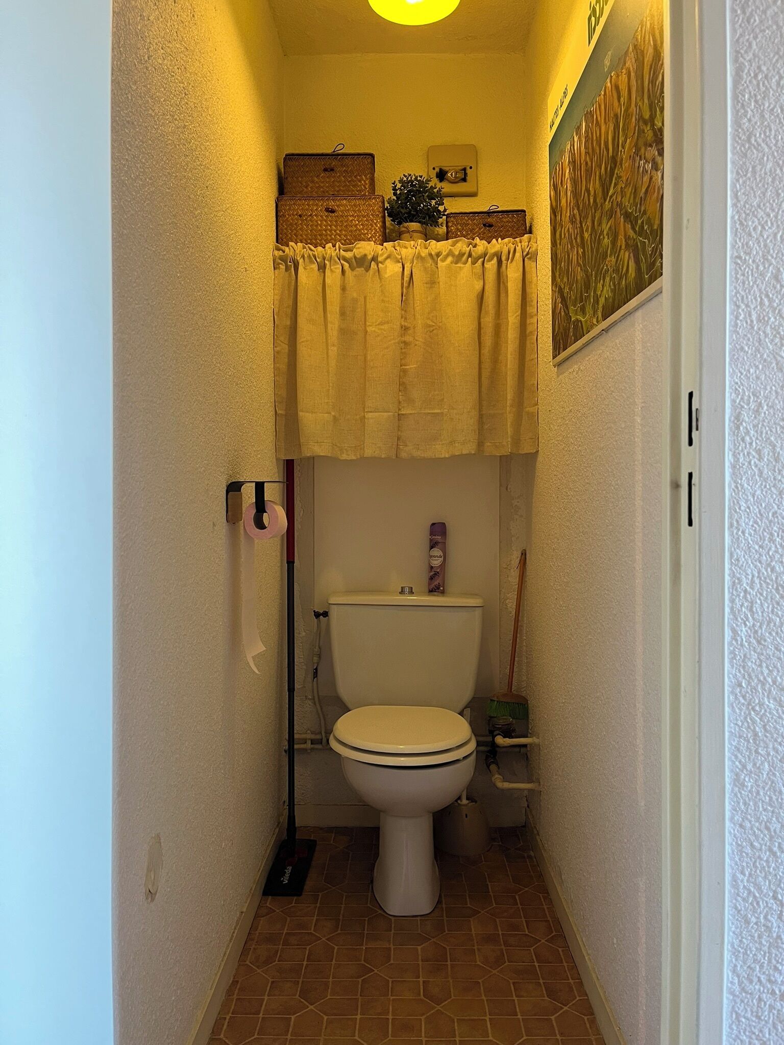 Un baño pequeño con inodoro, ducha y lavamanos. Hay un perchero y una pequeña repisa con artículos de aseo.