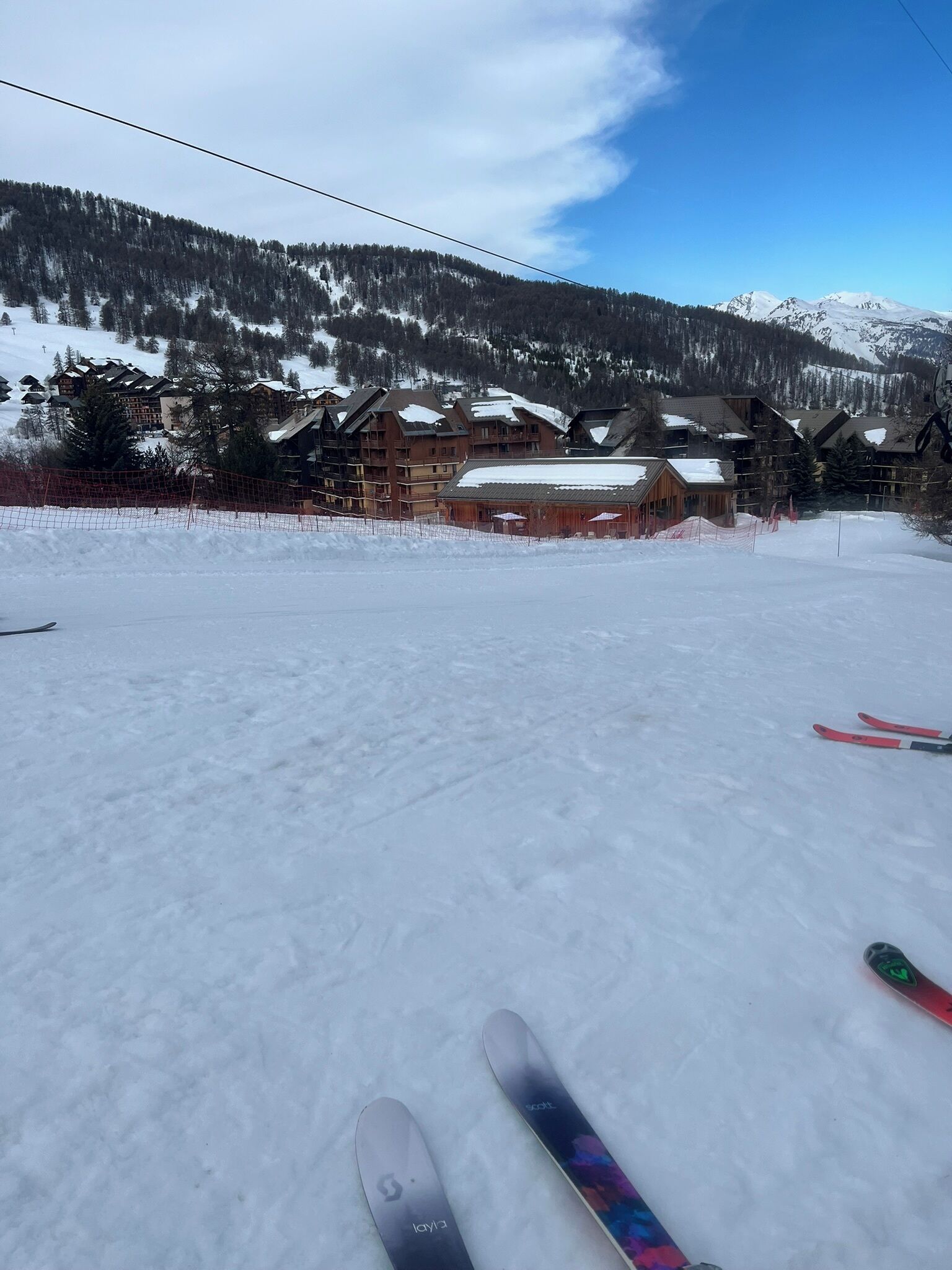 A snowy ski resort with wooden buildings, a ski slope, and a clear sky.