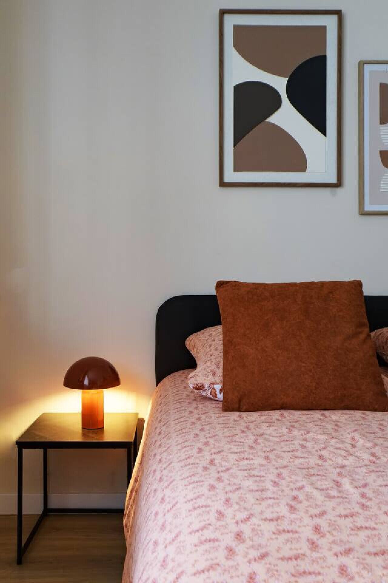 Une chambre à coucher avec un lit, une table de chevet, une lampe et une œuvre d’art abstraite accrochée au mur.