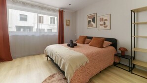 A bedroom with a bed, a bedside table, a lamp, and a window with curtains.