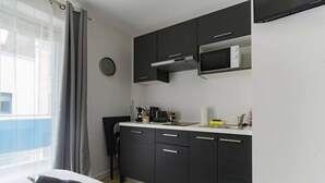 A modern kitchen with dark cabinets, a microwave, and a coffee maker. - Le 4B - Designer air-conditioned apartment in the city center (Vichy)