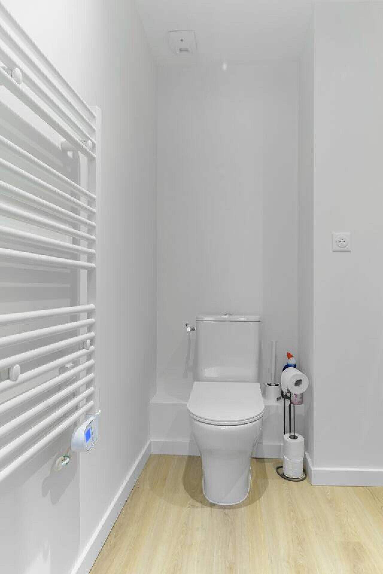 A small, modern bathroom with a toilet, a toilet paper holder, and a radiator.