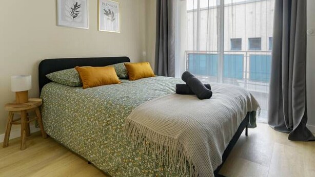 A bedroom with a bed, a nightstand, a window with curtains, and two wall-mounted pictures. - Le 4B - Designer air-conditioned apartment in the city center (Vichy)