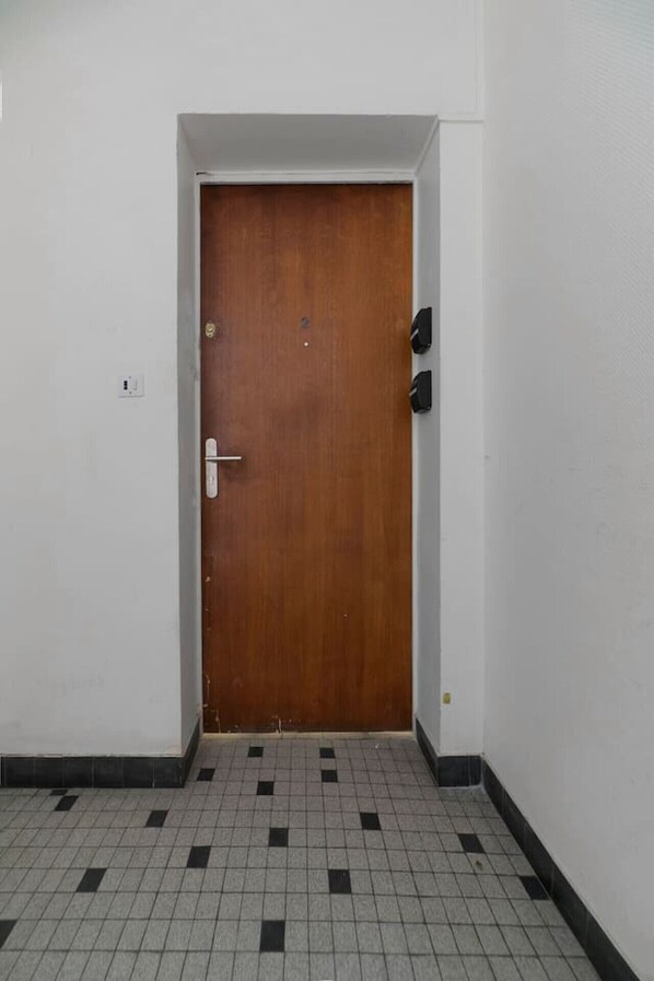 Un couloir avec une porte en bois, un sol carrelé et un mur blanc.