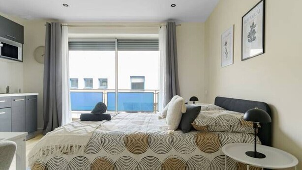 A modern bedroom with a bed, bedside table, and a view of the outside.
