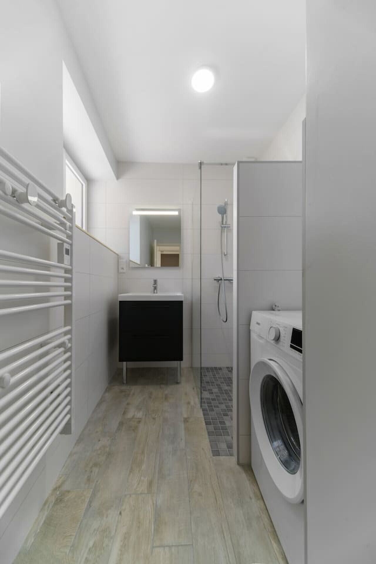 Un baño moderno con lavadora integrada, ducha y tocador con espejo.