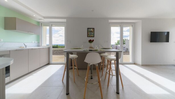 Een moderne keuken met een centraal eiland, barkrukken en een eettafel.