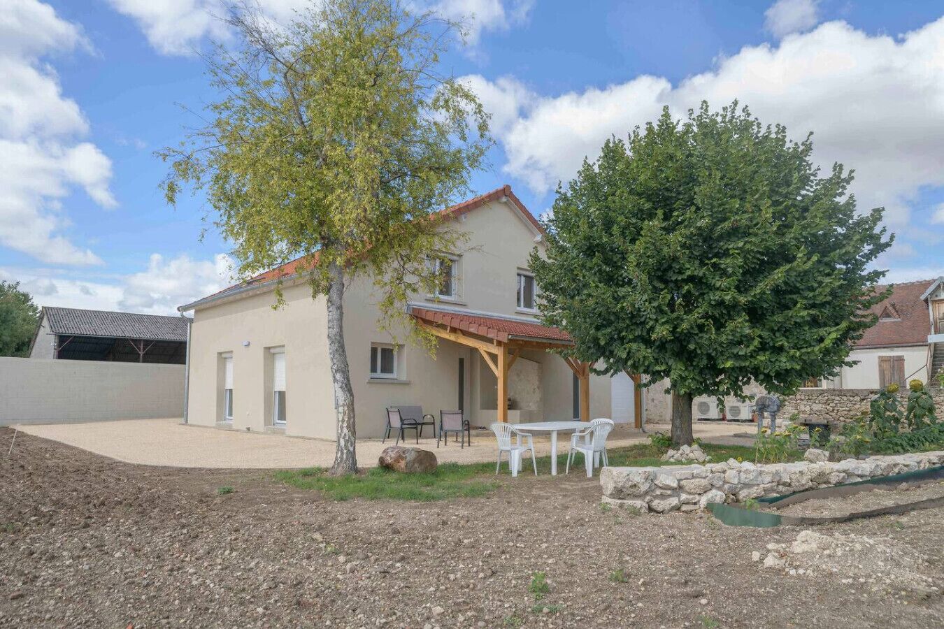 A two-story house with a patio area, a covered seating area, and a stone wall.