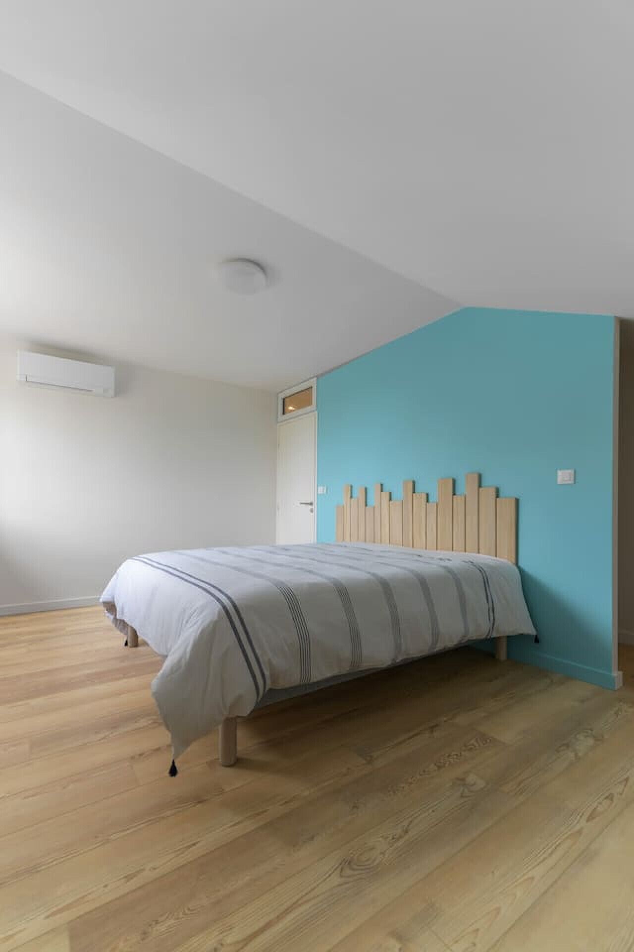 A bedroom with a bed, a white wall, a blue accent wall, and a wooden floor.