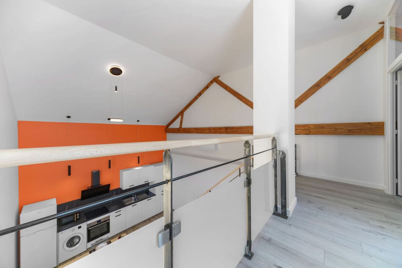 Una cocina moderna con horno y microondas integrados, techo con vigas de madera y una escalera con barandilla de metal.