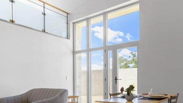 Ein geräumiger Raum mit hoher Decke, einem großen Fenster mit Blick zum Himmel, einem Esstisch mit Stühlen und einem modernen Sofa.