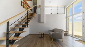 Ein modernes Interieur mit einer Holztreppe, einem grauen Sofa und großen Fenstern.