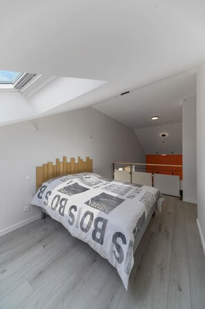 A bedroom with a sloped ceiling, a bed with a patterned bedspread, and a skylight.
