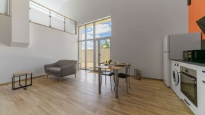 Ein großzügiger Wohnbereich mit grauem Sofa, einem Esstisch mit Stühlen, einer Waschmaschine und einem großen Fenster mit Blick zum Himmel.