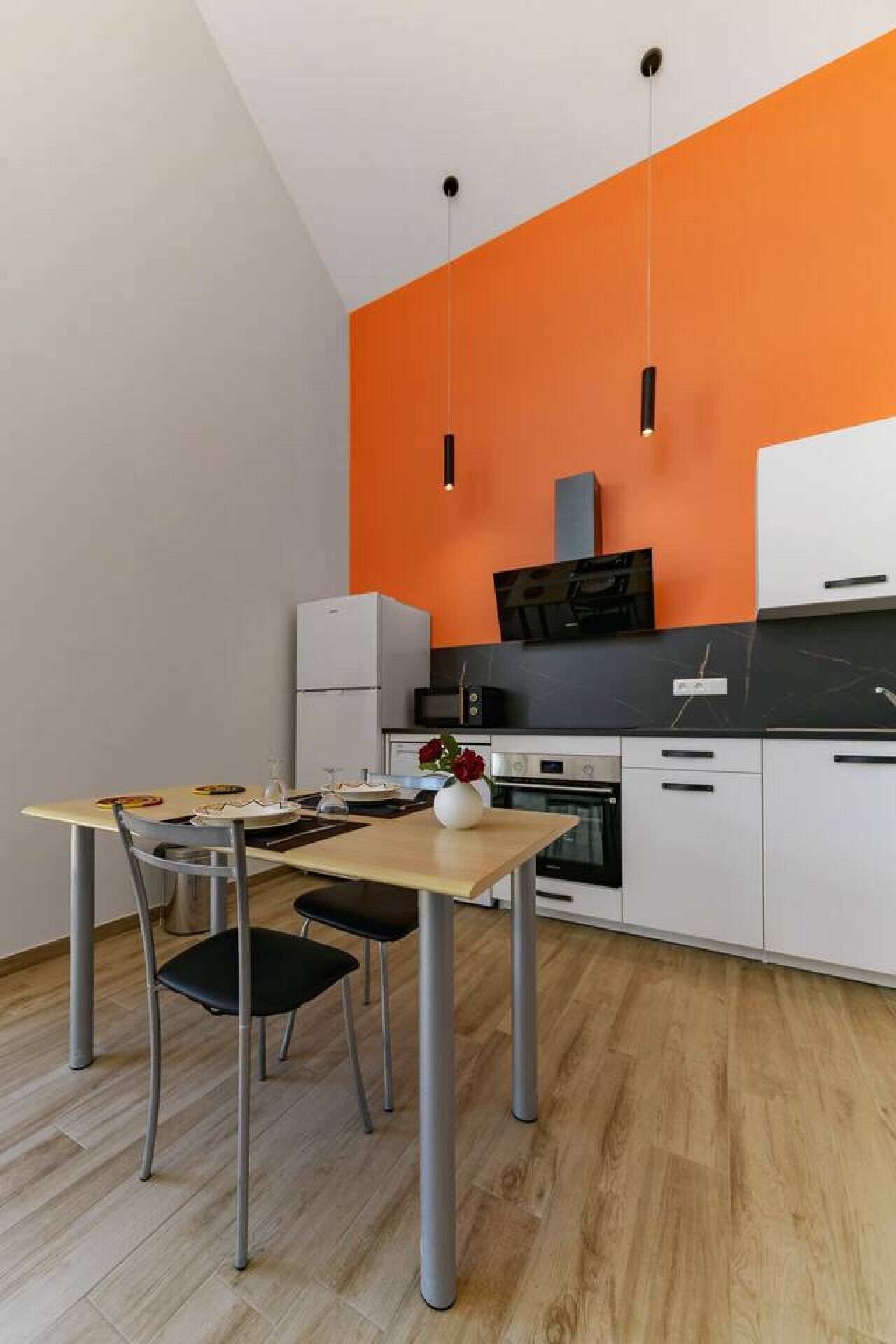 A modern kitchen with a wooden dining table, chairs, and a vase with flowers.