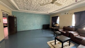 Een ruime woonkamer met een blauwe vloer, een plafondventilator, een bruine leren bank, een klein tafeltje en een televisie op de achtergrond.