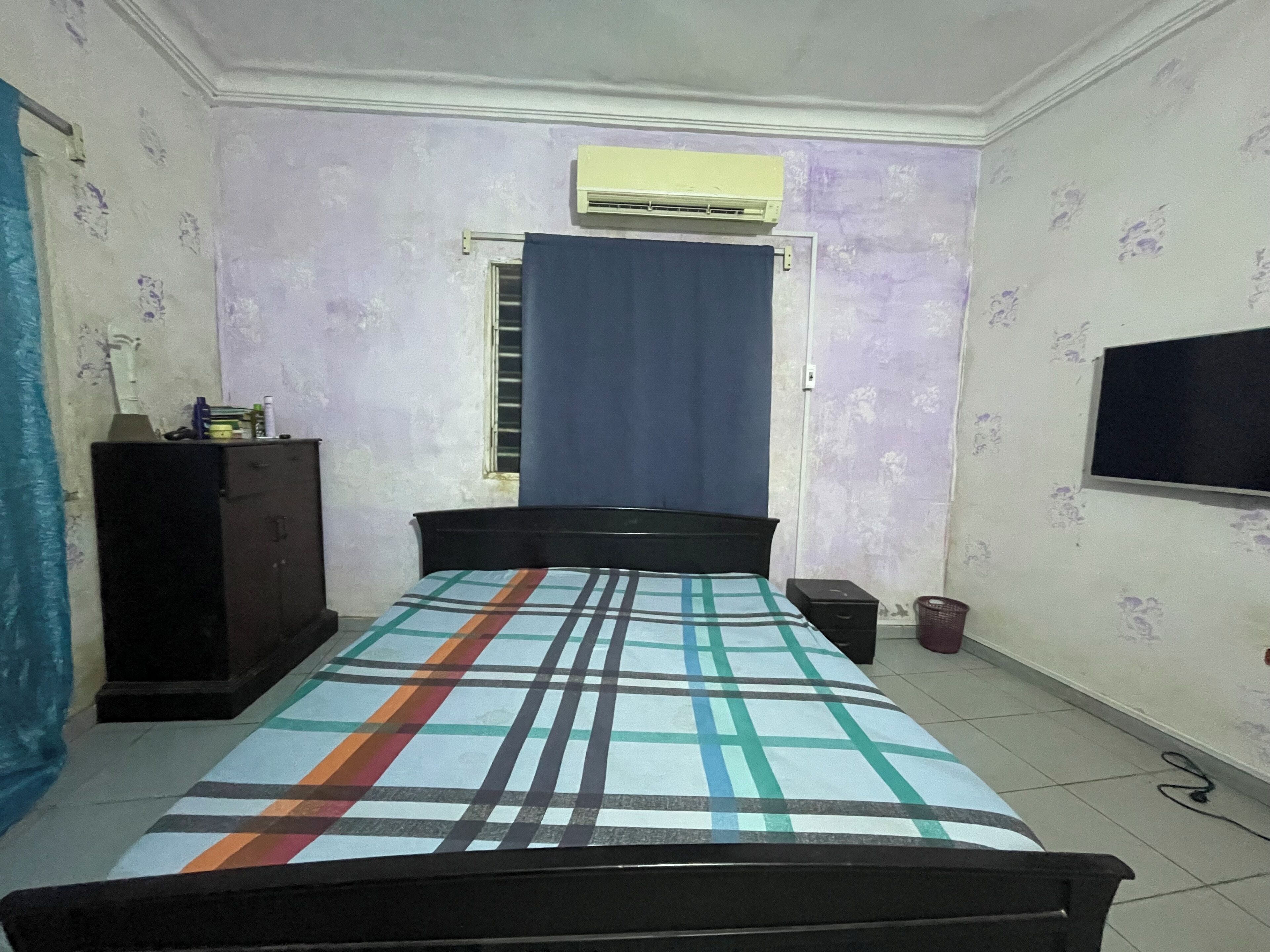 Une chambre avec un lit, une armoire, un appareil de climatisation, une fenêtre avec un rideau et un téléviseur fixé au mur.