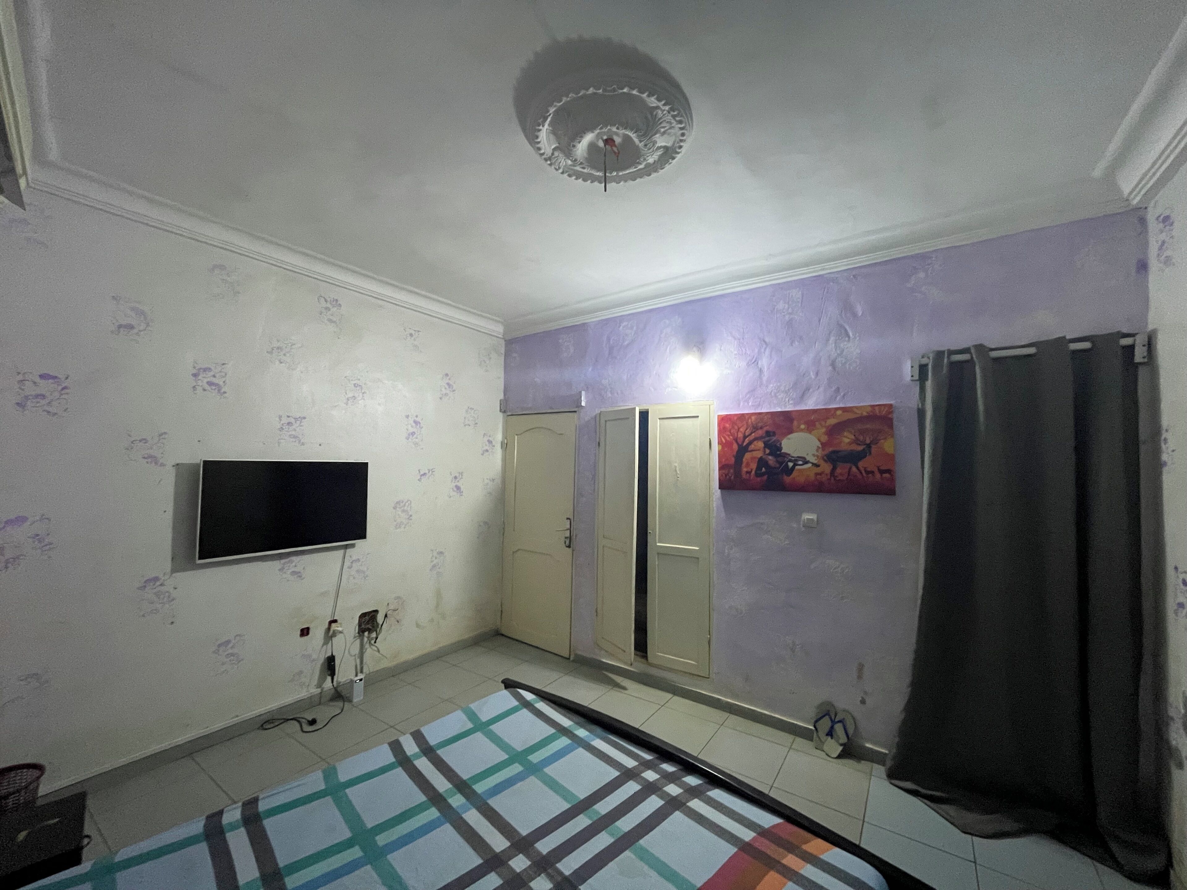 Ein Zimmer mit einem an der Wand montierten Fernseher, einem gemusterten Teppich, einer Tür und einem Bild an der Wand.