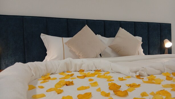 A bed with a dark headboard, white bedding, and yellow flower petals scattered on the surface. - De Sultana Villa (Muscat)