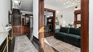 A spacious living area with a dark wood staircase, a green sofa, and a patterned rug. - Historic-11BR/7.5BA-Parking+By Metro+Chefs Kitchen (Washington)