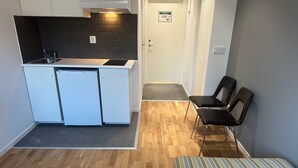 A compact kitchen with white cabinets, a black backsplash, and a built-in stove. There is a small seating area with two black chairs and a striped cushion. - Apartment 17 in Sollentuna (Sollentuna)