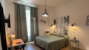 A bedroom with a bed, a desk with a chair, a small table with a plant, and a wall-mounted lamp. - Enjoy Rhome, your apartment just steps from the Basilica of Santa M. Maggiore (Roma)