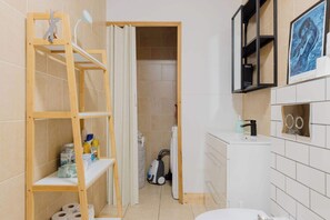 A bathroom with a wooden shelf, a toilet, a sink, and a shower area.