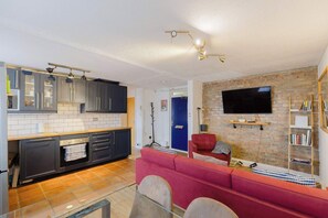 Eine moderne Küche mit grauen Schränken, einem roten Sofa und einem Flachbildfernseher an einer Ziegelwand.