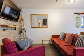 A living room with a TV, a mirror, a couch, and skateboards on the wall.