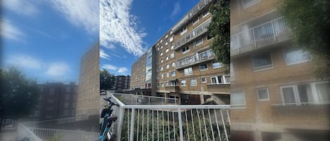 A multi-story residential building with balconies, a gated entrance, and a clear sky.