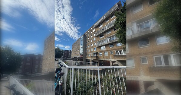 A multi-story residential building with balconies, a gated entrance, and a clear sky.
