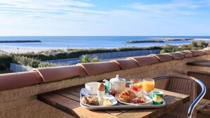 Bandeja de desayuno con cruasanes, huevos y jugo en un balcón con vista al mar.