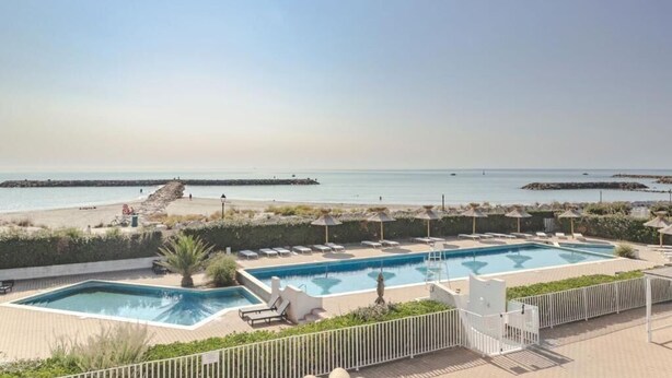 Zona de piscina con sillones de descanso y sombrillas, con vista a una playa y el mar.