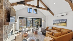A spacious living room with a high ceiling, stone wall, and large windows. There is a fireplace, a sofa, and a coffee table. - Luxury Mountain Retreat - Private Hot Tub and Walk to Lifts (Keystone)