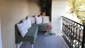 Un espacio de descanso al aire libre con techo, sofá verde, cojines blancos y una pequeña mesa con un florero.