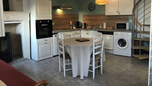 Cocina moderna con armarios blancos, horno empotrado, microondas y lavadora. Cuenta con una mesa de comedor, sillas y una lámpara colgante.