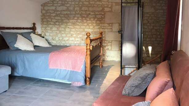 Un dormitorio con pared de piedra, una cama con cabecera de madera, un sofá y un ventanal corredera.