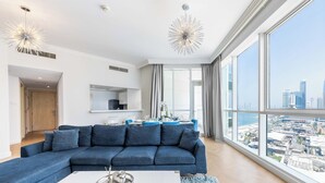 A modern living room with a large sectional sofa, a dining table, and a city view through large windows. - Al Bateen I Ultra Luxury I Private Beach (Dubai)